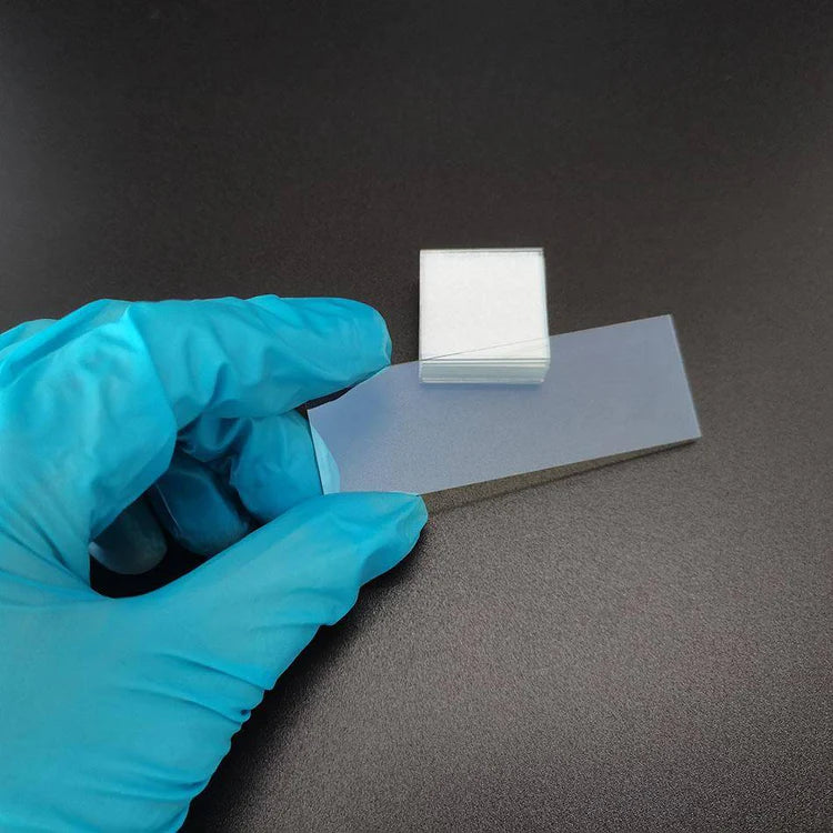 Laboratory sample of ITO conductive glass showing transparent conductive coating handled with gloves